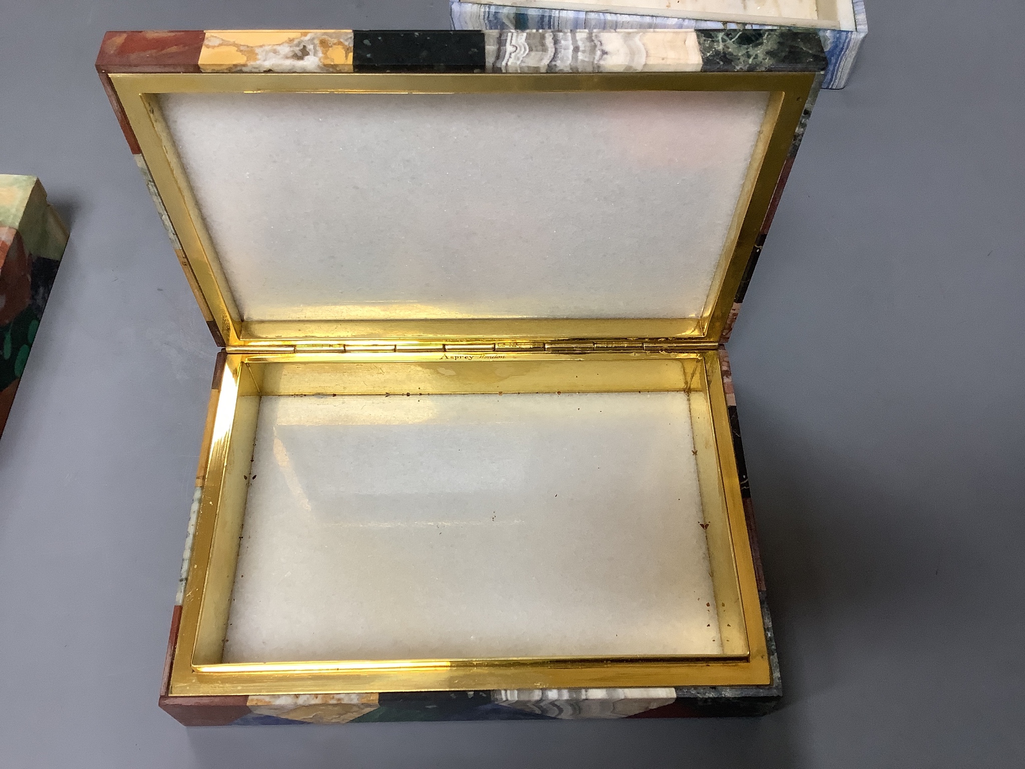 Two specimen marble cigarette boxes, 15cm and a similar blue agate cigarette box, 15.5cm, all three retailed by Asprey London and signed to the hinge mount
